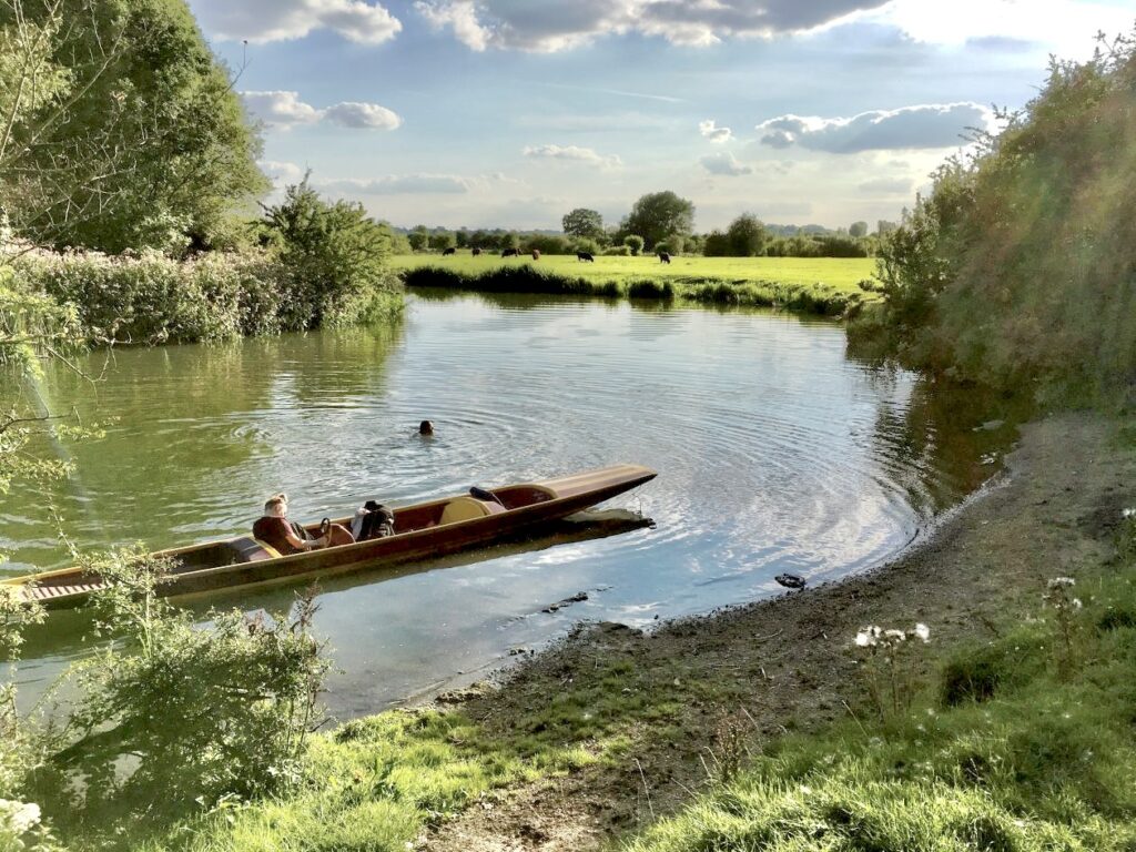 lievelijke rivier die naar links weg buigt met een roeibootje op de voorgrond en in de verte een zwemende vrouw