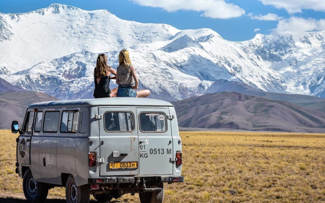 grijs busje met twee vrouwen erop die kijken naar de bergen in de verte