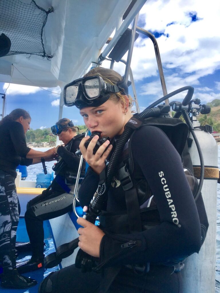 Meisje kijkt de lens in met een. duikbril en duikpak aan in een houten bootje