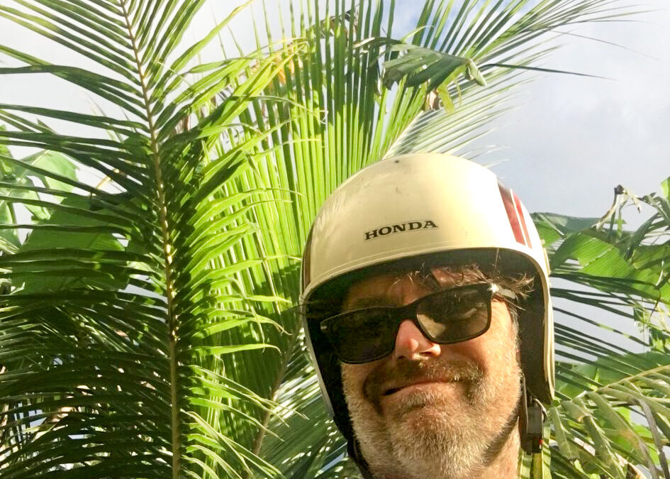 Man met hippe vintage motorhelm op zijn hoofd met achter hem een palmboom