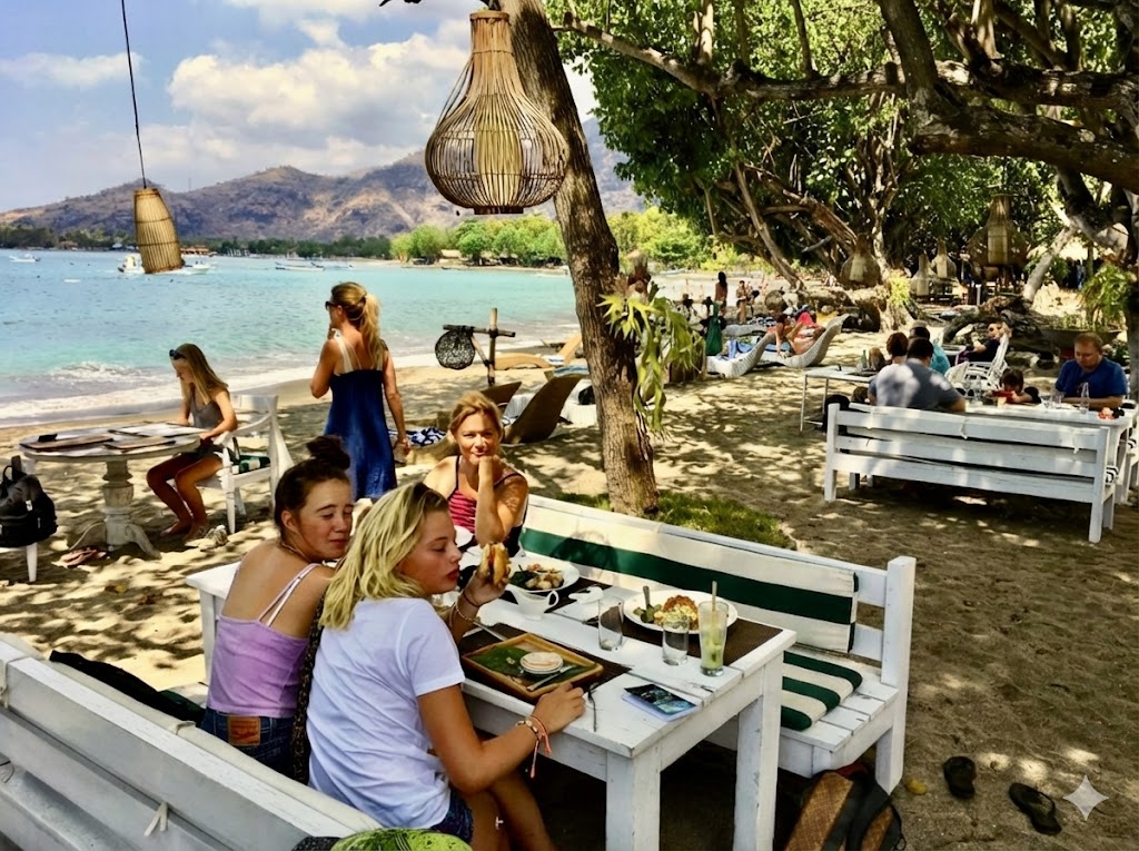 Restaurant op het strand met uitzicht op een baluwe zee met rechts een bomenrij voor de schaduw