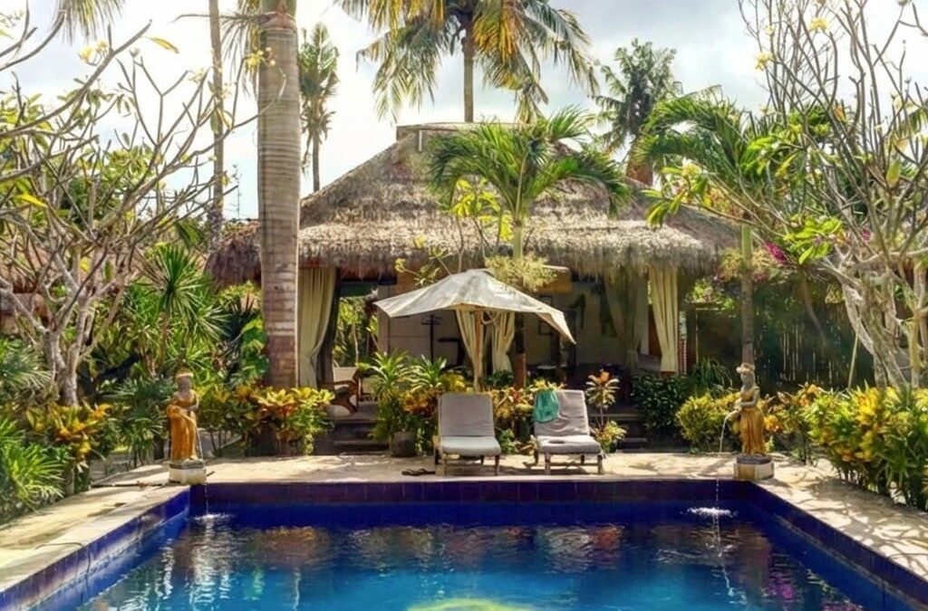 Zwembad met op de achtergrond een huisje in een tropische omgeving