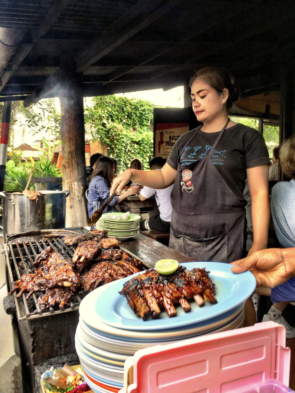 Vrouw staat onder een afdak spare ribs te braden op een bbq