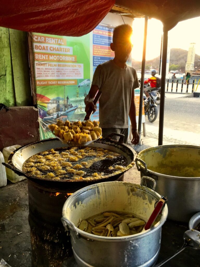 En man met tegenlicht frituurt bananen onder een afdakje