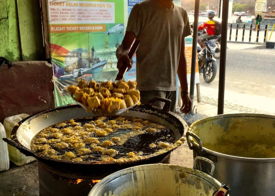 En man met tegenlicht frituurt bananen onder een afdakje