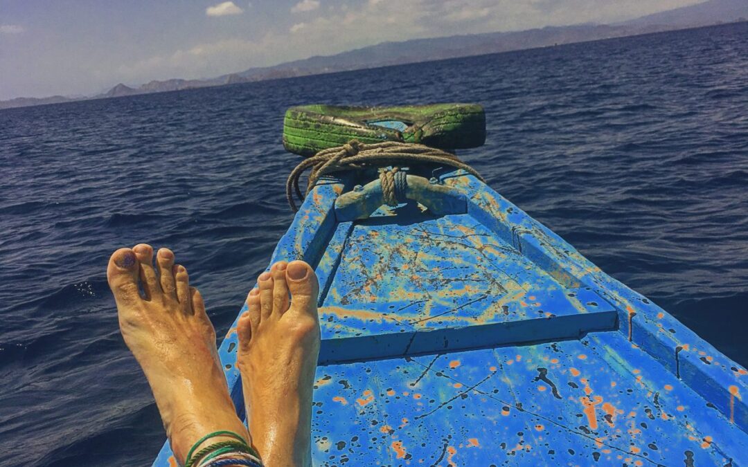 de punt van een blauw geschilderde houten boot . met twee benen die lui richting de horizan wijzen