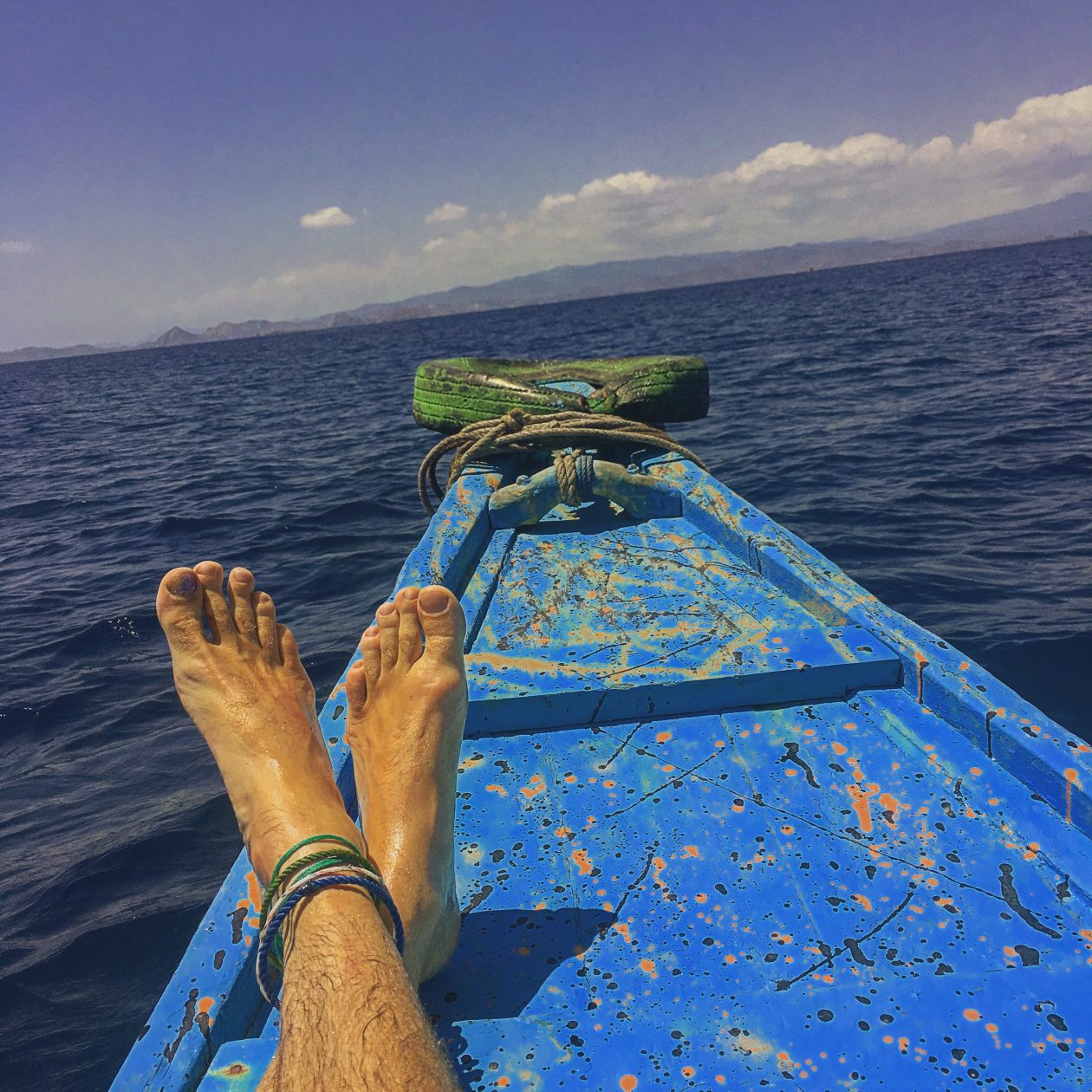 de punt van een blauw geschilderde houten boot . met twee benen die lui richting de horizan wijzen