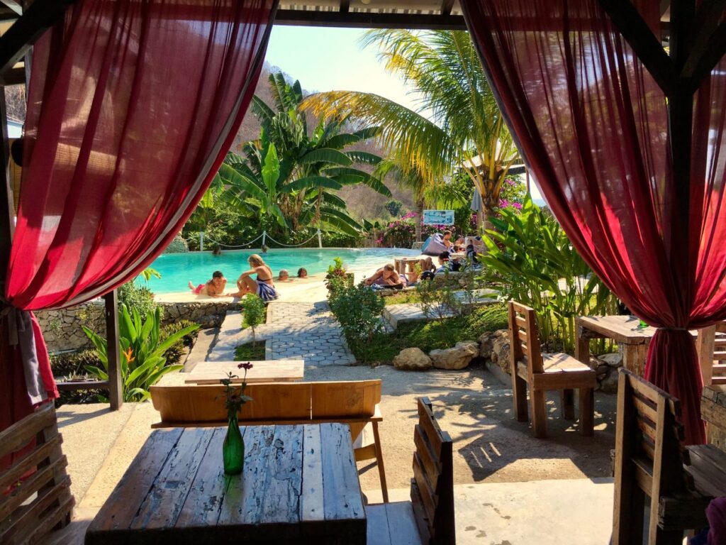Zwembad in tropische omgeving gezien vanuit een huis met rode gordijnen