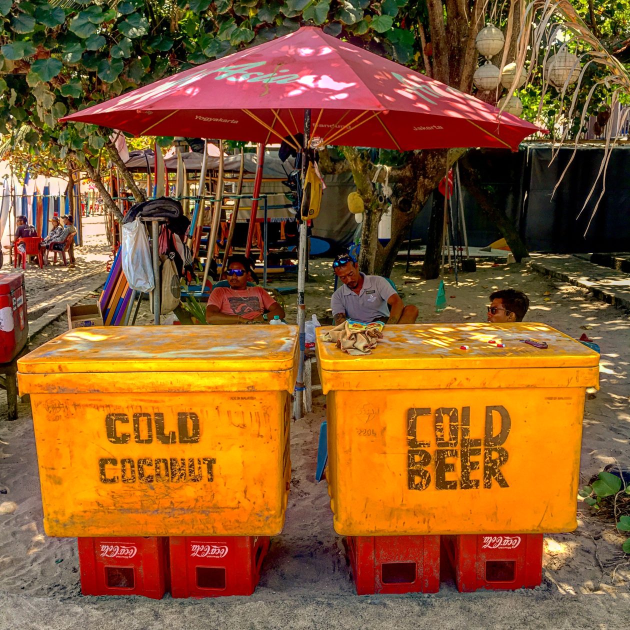 Twee enorme gele containers met bier op een strand met een parasol erboven