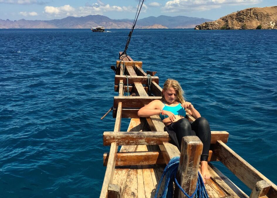 Meisje zit in de punt van een traditionle houten boot uit Indonesie op zee