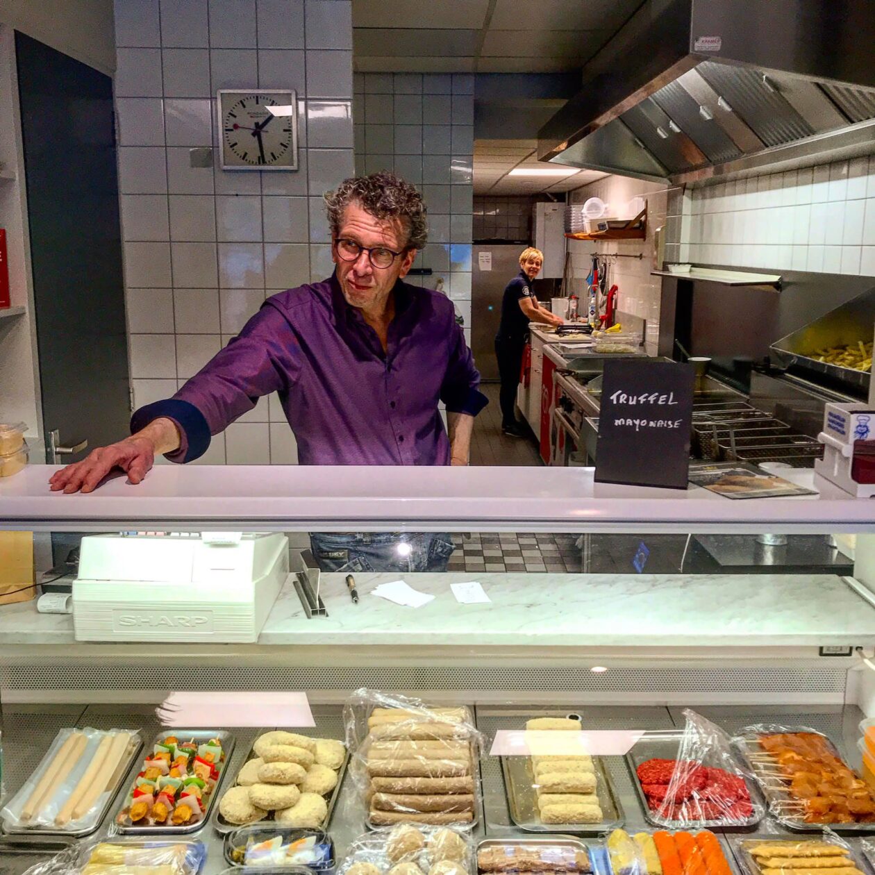 Man in Paars overhemd staat achter een snack vitrine