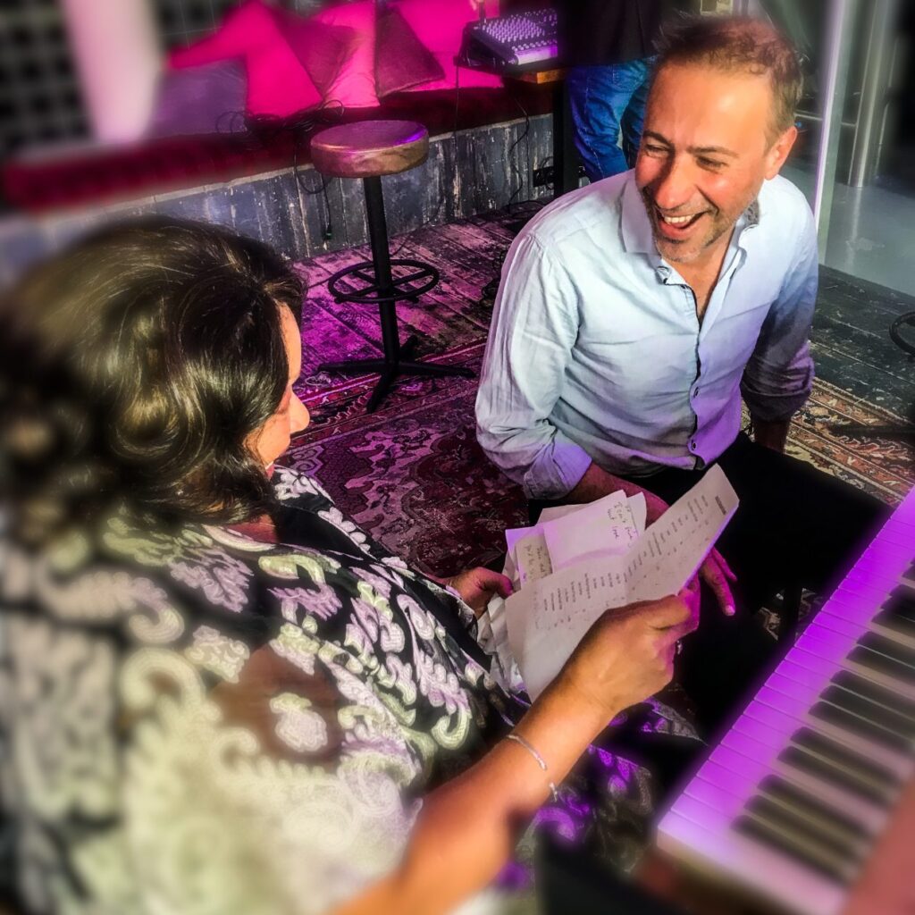 Man lachend achter de piano kijkt een vrouw aan die naast hem zit