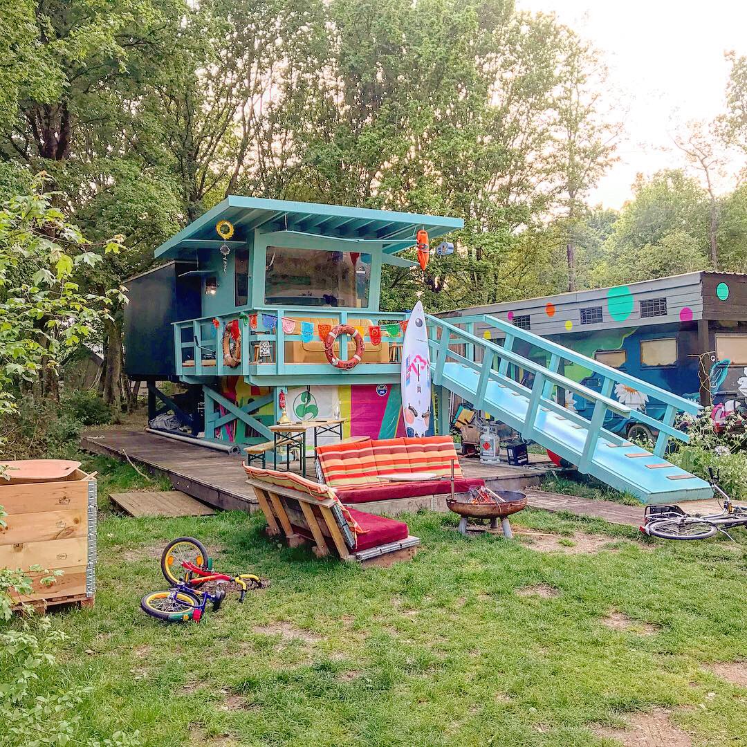 lichtblauw tinyhouse. met erachter een bos en ervoor een grasmat