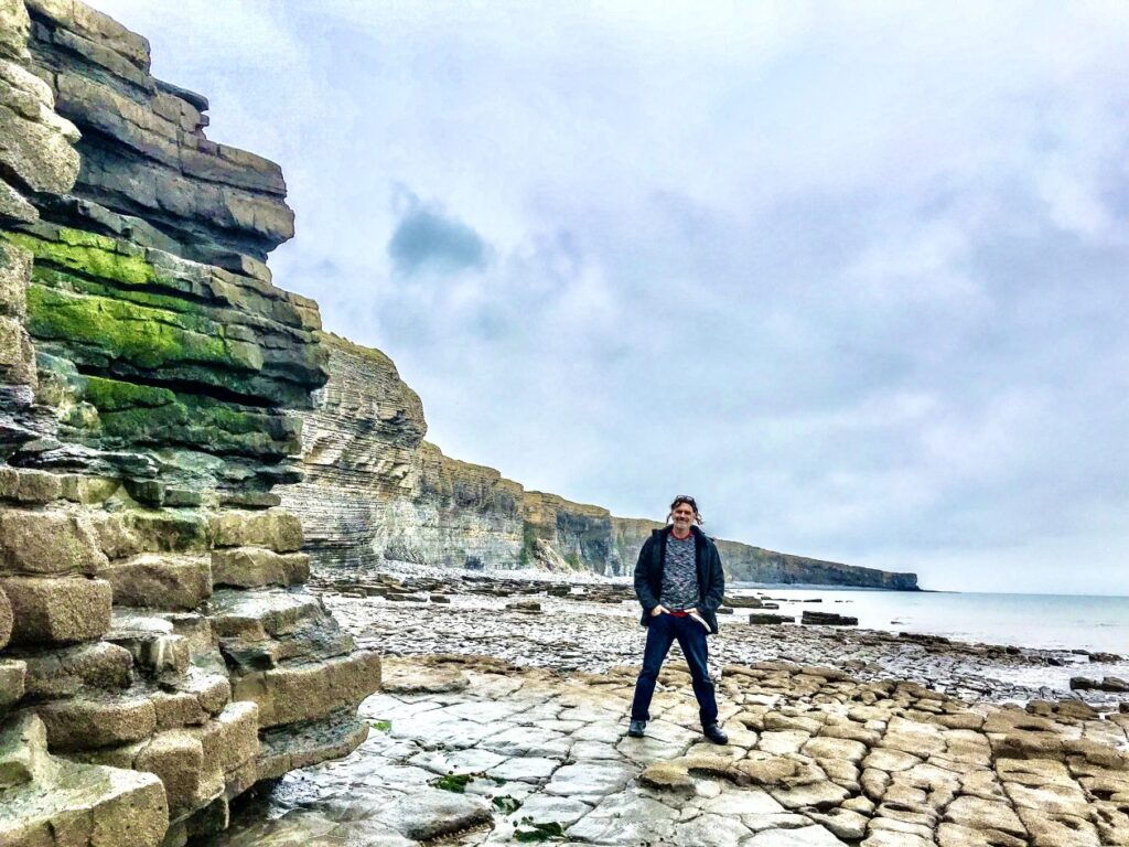 Man met links rotsen en rechts de zee in Wales