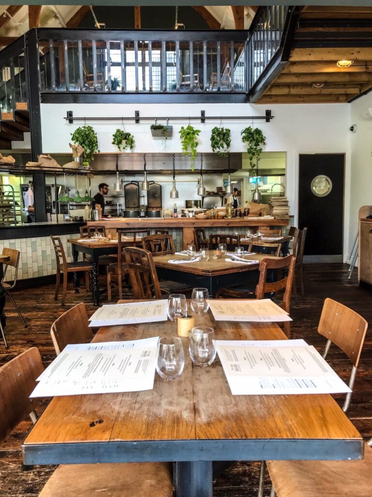 Gezellig restaurant met op de voorgrond een vier persoons tafel en aan het einde de bar