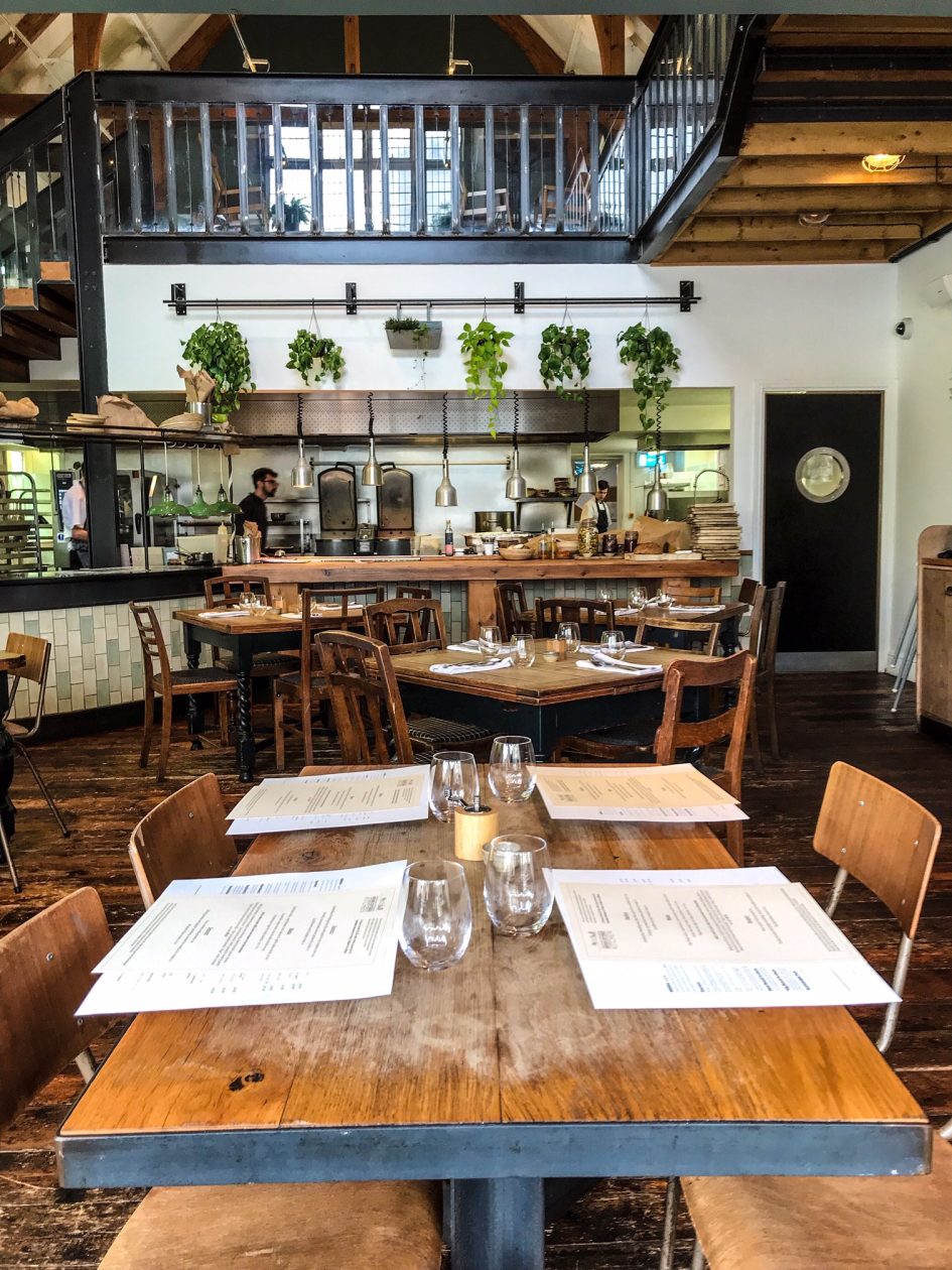 Gezellig restaurant met op de voorgrond een vier persoons tafel en aan het einde de bar