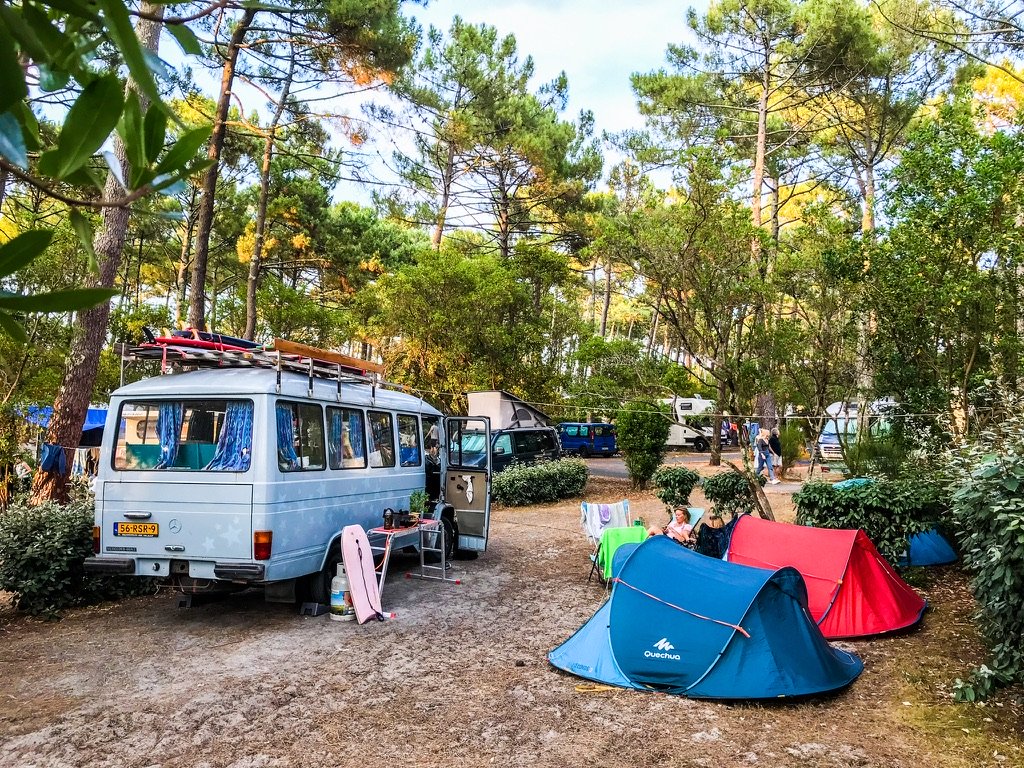 Vintage camper tussen de dennenbomen met twee tentjes ernaast
