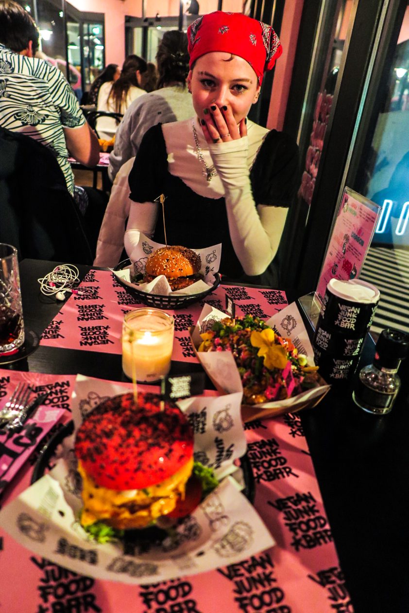 Een hamburger op de voorgrond , een meisje met een bandana houd haar hand voor haar mond