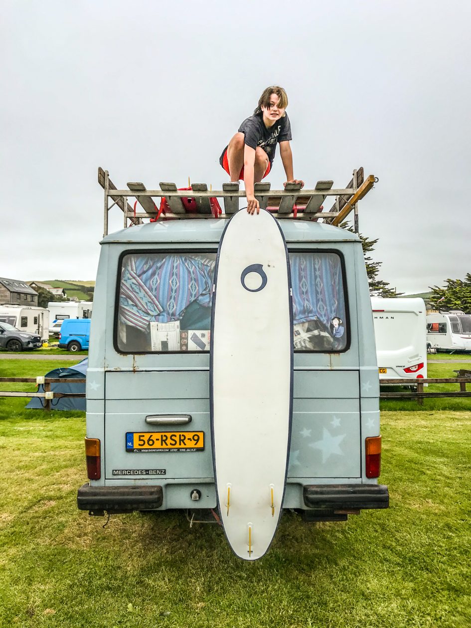 meisje boven op een camper laat haar surfboard zakken