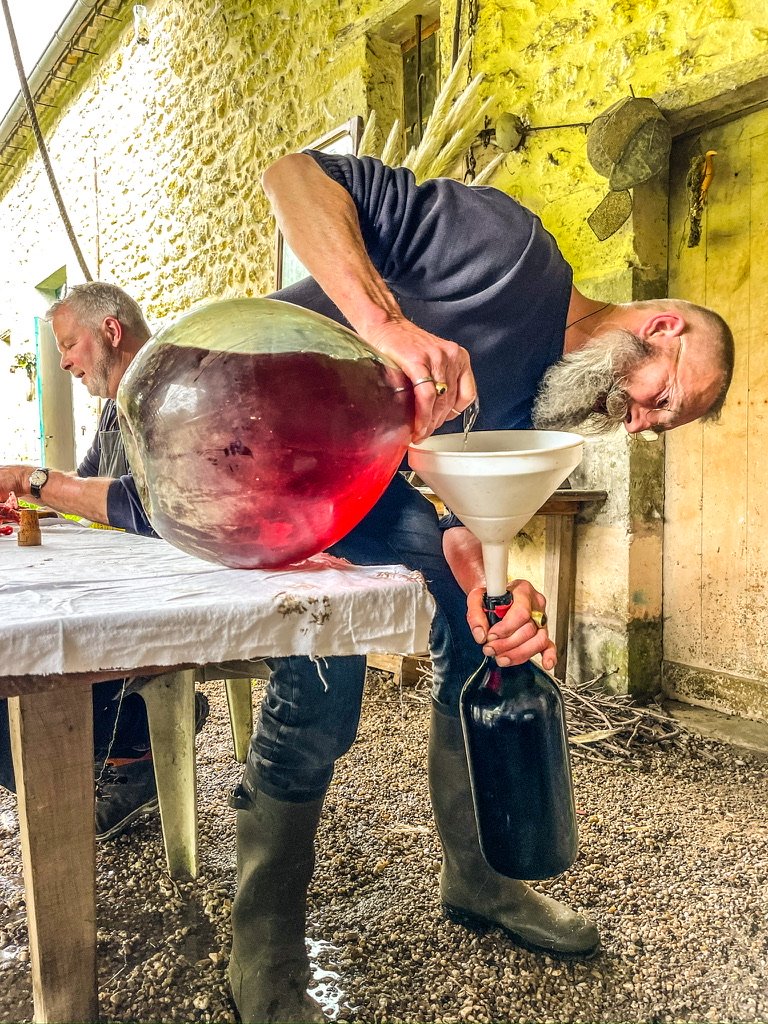 Man met een enorme fles bolle wijn schenkt hem voorzichtig uit in een kleinere fles