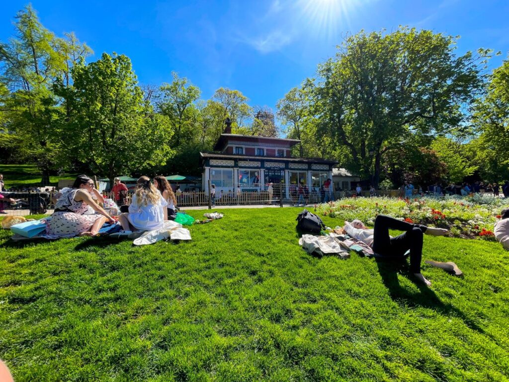 Park met in het gras luirende mensen en in de achtergrond een restaurant