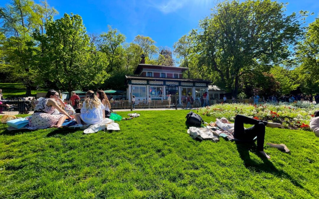 Park met in het gras luirende mensen en in de achtergrond een restaurant