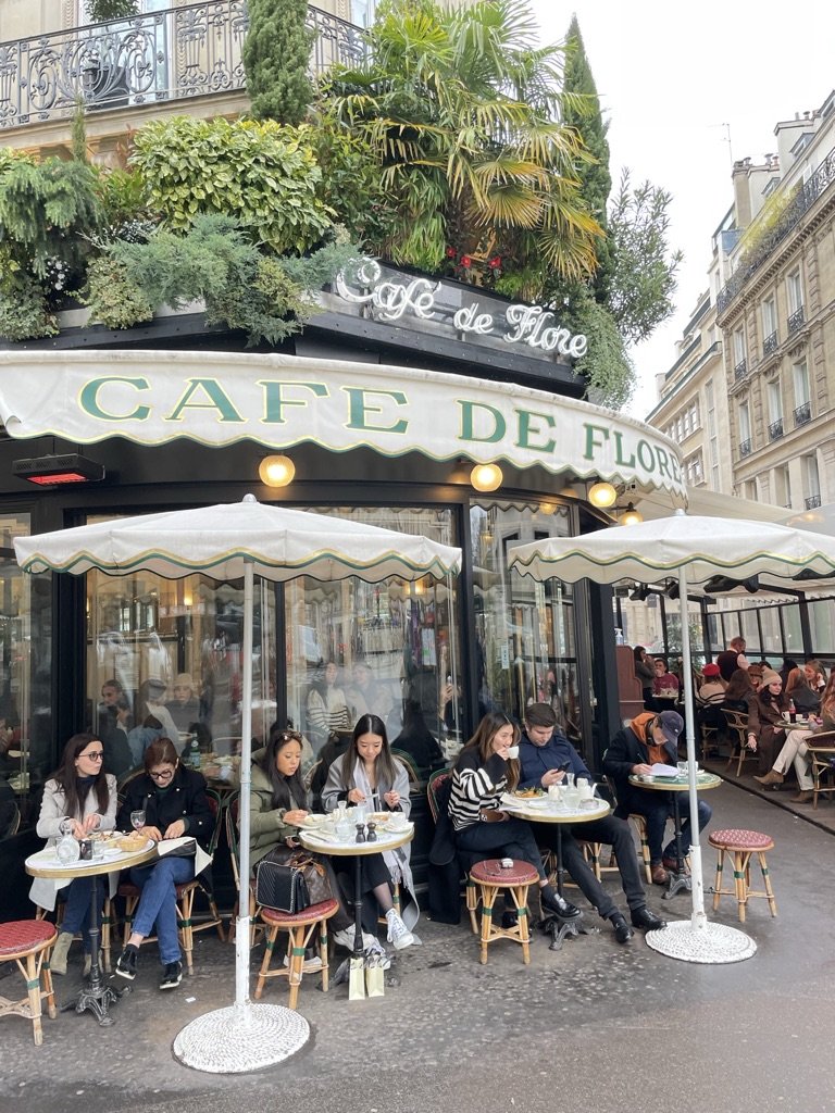 exterieur van Cafe Flore in Parijs mensen zitten onder de parasols