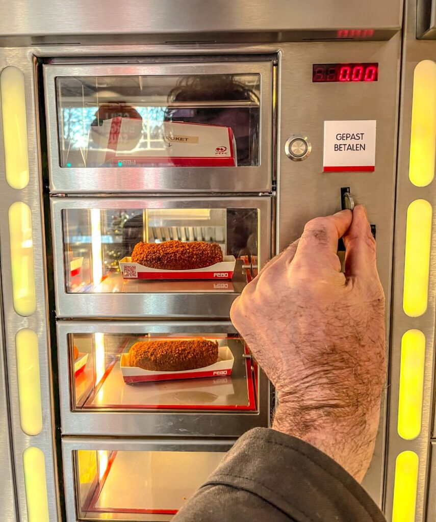 Hand die een muntje gooit om een sate kroket uit de "muur" te trekken