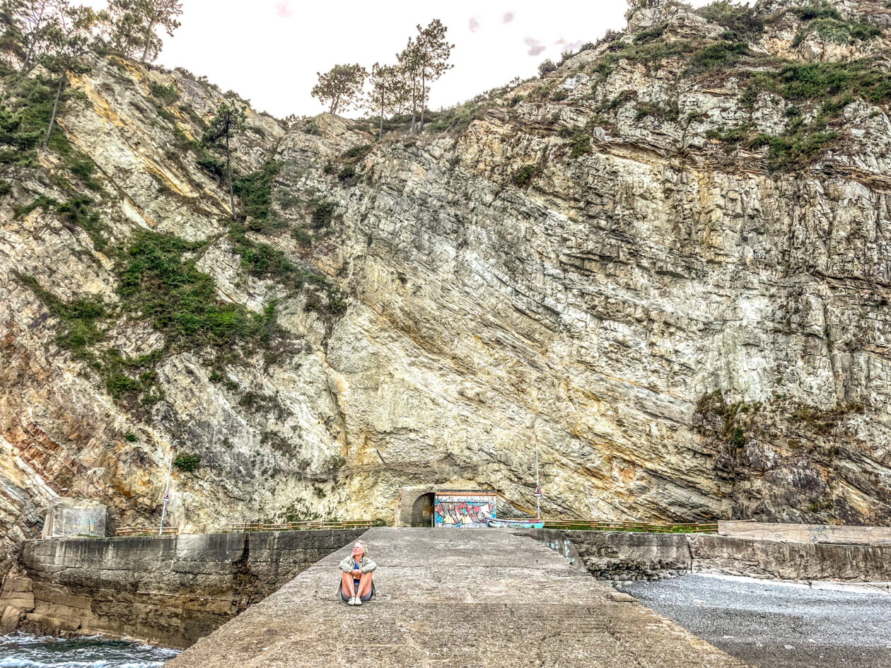 Betonnen pier in de zee met zittende vrouw en berg erachter