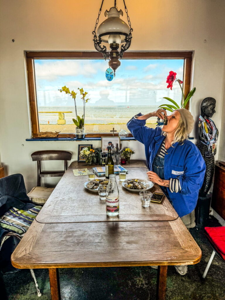 vrouw eet oester aan tafel met uitzicht op het wad
